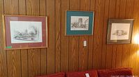 Three framed architectural prints hanging on wood-panel wall above a red couch
