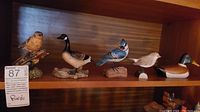 Five bird and duck statues displayed on a wooden shelf.
