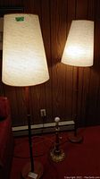 Two matching floor lamps with shades and one table lamp base grouped together against wood-paneled wall.