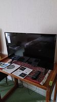 LG 32LJ500B TV on table with remote control and manuals placed beside it