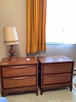 Frontal view of two walnut-tone nightstands side by side with lamp on left unit