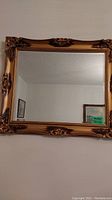 Gold ornate framed rectangular beveled mirror hung on wall.