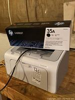 HP LaserJet P1005 printer with HP 35A toner cartridge box on top, showing front and side of printer and toner box.