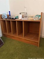 Front view of wood veneer cabinet with various decorative items on top, showing five vertical storage compartments.