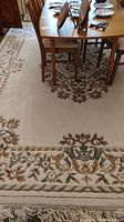 Full view of rug under dining table showing cream background and floral border