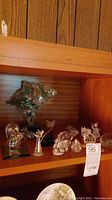 Shelf display of various Swarovski crystal and glass figurines including owl, mouse, angel, cat, and abstract glass art pieces