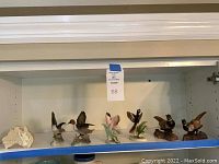 Shelf showing six ceramic bird figurines of various styles and poses arranged in a row
