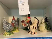 Photo showing five ceramic chicken and rooster figurines on a white shelf with a MaxSold tag.
