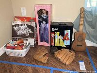 Full lot displayed showing chess set box, boxed collector's doll, black Barbie wardrobe box with Barbies, two baseball gloves, soft ball, and wooden ukulele.