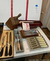 Photo of multiple boxed cutting utensil sets including steak knives, carving knives, and wooden cutting utensil block arranged on the table.