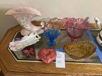 Lot of vintage glassware and pottery including a pink Hull Cornucopia vase and multiple colorful glass candy dishes arranged on a mirrored surface.