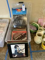 Top view of plastic bin holding multiple vinyl LP records showing album covers of Aerosmith and Billy Squier.