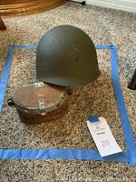 Photo showing military helmet and gas mask canister inside blue tape perimeter on carpeted floor.