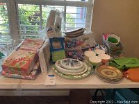 Photo of assorted party supplies on table including stacks of paper plates, floral and patterned napkins, plastic cutlery banded in packaging, ice cream bowls, and plastic ice cream scoop.