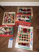 Five boxes of vintage Shiny Brite Christmas tree ornaments arranged on a floor showing different packaging and ornament styles.