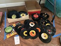 Vintage 45 RPM records scattered on floor with cardboard boxes and Disney illustrated sleeve visible
