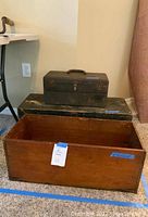 Smaller metal box with handle on top, sitting on top of large wooden box, showing front latches and keyhole.