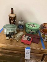 Wide view of all vintage collectible items on wooden surface displaying tin, Barbie wallet, decorative stein, cologne bottle, ceramic train car, and other small collectibles.