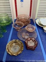 Photo showing assortment of vintage colored glass dishes, including pink plates, gold-toned ruffled bowl, ruby red bowl, green footed dish.