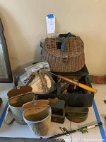 Full view of vintage fishing gear assortment including basket, tackle box, creels, anchor and rods