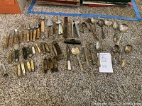 Overview of lot showing bone-handled folding utensils, pocket knives and spoons laid on carpet