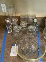 Clear glass storage boxes, vases, canisters and bowls grouped on a counter with blue tape outline