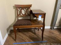Front view of the vintage wooden gossip table showing the upholstered seat and decorative backrest.