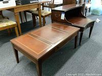 Rectangular coffee table with dark mahogany wood frame and leather top with decorative gold tooling, showing wear and missing drawer pull