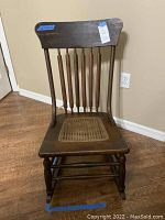 Front view of vintage wooden rocking chair showing vertical spindle backrest and cane seat.