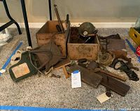 Full view of assorted vintage tools including wooden boxes, hand drill tools, metal funnel, anvil, and other rustic metal tools