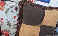 Photo showing the front side of both toss pillows, highlighting the floral pattern pillow and the brown and tan patchwork pillow with fringe and button detail.