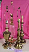 Four vintage solid brass lamps against pink backdrop, showing full height and detail of lamp tops and bases