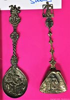 Top view of two antique silver plated decorative spoons, showing ornate handles and embossed bowl designs.