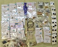 Full overview of lot contents showing multiple packaged necklaces, bracelets, earrings, and jewelry making parts arranged on a surface.