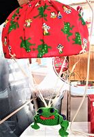 Overall lamp showing red fabric shade with green frog and mushroom print, plus hanging plush frog mobile.