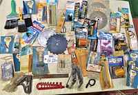 Lot overview photo showing assorted brushes, blades, tapes, hardware parts, and small tools arranged on a white surface