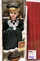 Image showing the vintage Dynasty Doll Genevieve in original box, dressed in dark green velvet dress with white lace, with stand and tag visible.