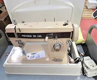 Front and top view of vintage Precision Zig Zag sewing machine model YDK YM-43 in beige color. Machine is in original case with attached foot pedal visible. Light indicator on machine is on.