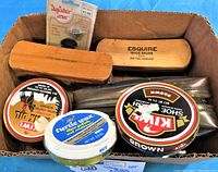 Shoe shine kit contents with brushes, shoe polish tins, and repair kit parts in cardboard box.