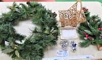 Top view of the lot showing faux pine wreath with green leaves and berries, woven star basket, angel bell set, and smaller faux pine decoration with red berries and pine cones. White surface background with measurement ruler.