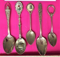 Photo showing all five collectible vintage souvenir spoons laid out on a pink background. Details include the U.S. Capitol building, rose floral design, colonial engraving, and ornamental handles.