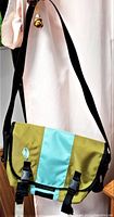 Front view of vintage Timbuk2 messenger bag showing aqua light blue and dusty lime green color panels with black adjustable shoulder strap and buckle closures.