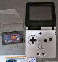 Overhead photo showing silver Game Boy Advance SP with screen flipped up and Mega Man Zero 2 cartridge inside protective plastic case to its left.