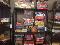 Photo showing various board games stacked on metal shelves including Stratego, Risk, Pente, Payday, Battleship.