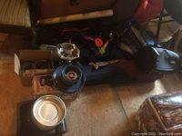 Photo of camping gear collection with backpacks, portable stoves, and sleeping bag visible on wooden floor.