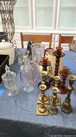 Table with brass candlesticks, amber glass candlesticks, clear glass vases, and decor items on blue tablecloth