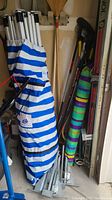 EZ UP canopy in striped blue and white bag leaning against wall, boat anchors and ski poles behind