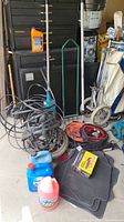 Photo showing various automotive accessories including floor mats, fluid containers, coiled cables, tree stand, and jumper cables in garage setting.