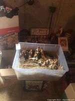 Plastic bin with ceramic nativity scene figures inside, including Holy Family and animals, arranged with straw inside the bin.