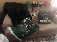 CSU sports flag in green and white, assorted clothing including CSU apparel pieces on a couch along with four western-style hats and two decorative pillows